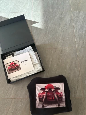 Svart hoodie Limitato  - Svart hoodie från Limitato med en stor, färgstark print på bröstet som visar en bil och en person i röd outfit. Hoodien har dragsko i huvan och ribbade muddar.