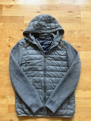 Grå massimo dutti cardigan - Snygg grå massimo dutti jacka med quiltad framsida och rygg samt stickade ärmar och huva. Jackan har dragkedja framtill och två fickor med dragkedja. Perfekt för kalla dagar när du vill hålla stilen och värmen. Skriv om ni har någea funderingar:)