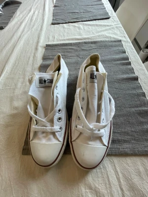 Vita Converse All Star låga sneakers - Klassiska vita Converse All Star sneakers i lågt snitt med vit canvas, vita snören och gummisula med röd rand. Ikonisk logga på plösen och metallöljetter för snörningen. Perfekta för en avslappnad och stilren look. Defekt vid sulan (se bild 3)