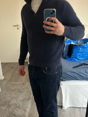 Mörkblå halvzip tröja - Säljer en mörkblå stickad tröja med halvzip och hög krage. Tröjan har ribbade muddar vid ärmslut och nederkant, och är långärmad. Perfekt för dig som gillar en enkel och stilren look.