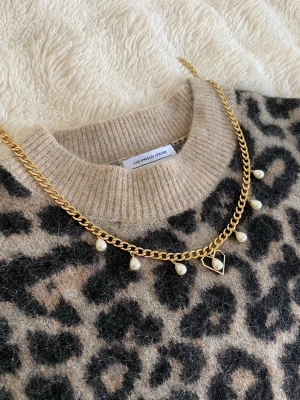 Guldhalsband med pärlor och hjärta - Snyggt halsband i guldfärgad rostfritt. Kedjan har små vita pärlor som hängande detaljer och ett öppet hjärthänge . Perfekt accessoar för att lyfta vilken outfit som helst med en trendig touch.