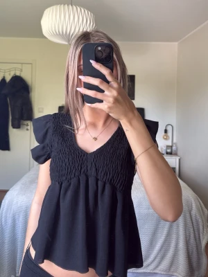 Svart blus med volangärmar - Söt svart blus med smock upptill och volangiga korta ärmar. Köpt i en butik i Spanien 