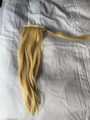 Blond löshårspjäs med clip-in - Säljer en lång, vågig hårförlängning i blond nyans med clip-in fäste. Perfekt för att snabbt få längre och fylligare hår. Materialet känns mjukt och naturligt, och passar dig som vill ha en enkel stylinglösning.
