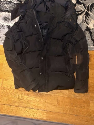 Svart dunjacka från Canada Goose - Säljer en svart dunjacka från Canada Goose med klassisk patch på ärmen. Jackan har dragkedja och knappar framtill, två sidofickor med dragkedja och en hög krage. Perfekt för kalla vinterdagar och riktigt varm tack vare dunfyllningen.