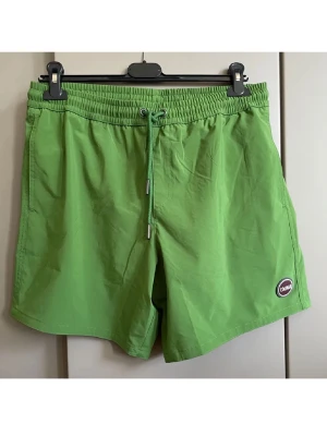Gröna badbyxor från Colmar - Snygga gröna badbyxor från Colmar med elastisk midja och dragsko. Klassisk modell med sidofickor och en bakficka med lock. Tillverkade i snabbtorkande material, perfekta för stranden eller poolen. Colmar-logga framtill.