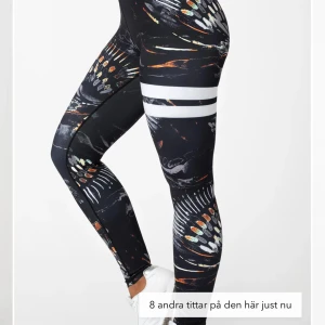Svarta leggings från Stronger - Svarta leggings från Stronger med ett färgglatt mönster som liknar fjädrar eller penseldrag i vitt, orange och grått.   Mycket populära & sjukt bra kvalite!  OBS! finns ett mycket litet hål, som jag sytt igen.
