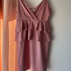 Rosa klänning - Rosa klänning med volanger över midjan, lite ät de gammeldags rosa hållet. Tyvärr har ett armband fastnat i ena sidan och den har blivit lite nopprig. (Se bilder). Använd en gång, storlek s