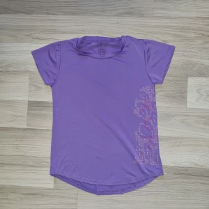 Lila t-shirt - En lila t-shirt med korta ärmar och ett tryck på sidan. T-shirten har en rund halsringning och är tillverkad i ett mjukt material. Från ellos i stl 164