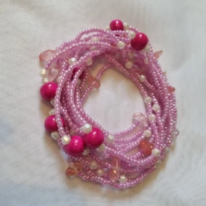 Rosa pärlhalsband - Ett långt rosa pärlhalsband med små och stora pärlor i olika nyanser av rosa och vitt. Halsbandet har flera rader av små rosa pärlor med inslag av större rosa och vita pärlor.