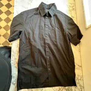 En svart kortärmad HM skjorta med storlek XS i passformen relaxed fit. En tunn skjorta som är perfekt i sommarvädret. Använts endast 2-3 gånger så funkar precis som ny. 