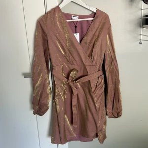 Sommarklänning - Klänning från Noisy May, aldrig använd. Klänningen är gammelrosa med guldigt glitter/skimmer inblandat. Ser magiskt ut i solen och bra ljus😍 Knytning i midjan och lite piffigare armar. Prislapp är kvar, nypris 500kr