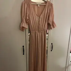 En superfin v-ringas rosa jumpsuit / byxdress i satin med knappar framtill samt smock vid axlarna och kort puffärm med volang från H&M i strl 34!💓