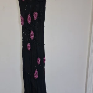 Festklänning köpt från England  - Otrolig slip dress  Ceriserosa blommor och pärlbeströdda broderier, draperad urringning och tunna axelband. Dessutom asymmetrisk kjolskant med långa fransar av pärlbeströdda . Lite stretchig, passar storlek XS och S.  Som referens har jag vanligtvis 