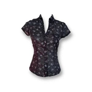 Svart skjorta - En  svart skjorta med ett mönster med kassettband i vitt. Skjortan har korta ärmar och knappar framtill samt ett band i midjan för bättre passform. Fint skick!