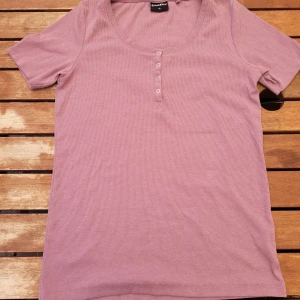 Rosa ribbad topp från Newbie - En rosa ribbad topp från Newbie med korta ärmar och rund halsringning. Toppen har knappar framtill för en dekorativ detalj.