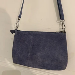 Blå axelremsväska - Säljer denna blåa axelremsväska i mocka. Köpt på plick så vet tyvärr inte vilket märke. Den är i använt skick så därav priset :)