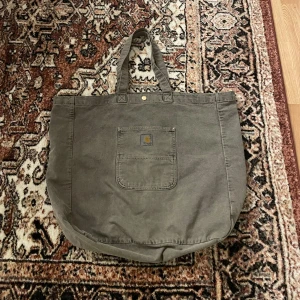 Carhartt tote bag - Släpper den här jätte fina totebag från carhartt! Använd en gång. 800 sek nypris. Den är stor så finns gott om plats. Går att stänga med en knapp och har ett fack på insidan. Hojta till om du är intresserad, pris inte hugget i sten😃