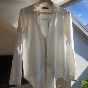 Skjortblus med ryggdetalj - Längre framtill, kortare och omlott/öppen i ryggen.  Cremevit  Använd fåtal gånger.  XS från Åhléns. 