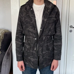 Sandro Paris Field Jacket  - Otrolig Field jacka från Sandro Paris i ett mörkt grått militärmönster.   Jackan är i storlek XS och personen på bilden är 179cm lång.   Jackan är i mycket fint använt skick. 