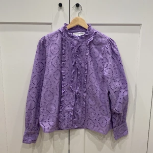 Lila blus med hålbroderier - Detta är en jättefin lila blus/skjorta som har hålbroderier, är i jättebra skick och är även lite liten i storleken så skulle passa storlek M.