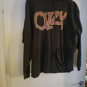 Ozzy-huvtröja  - Välanvänd. Fickan på magen är lite trasig, se bild. Trycket är lite sprucket. Bredd ca 60cm, längd ca 70 cm.
