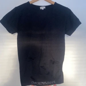Armani T-shirt  - Svart Armani T-shirt med logga på fållen och sidan. Stretchigt material.  Mått: Armhåla t botten 35cm Armhåla t armhåla 39,5cm Krage t botten (baksida) 56cm 