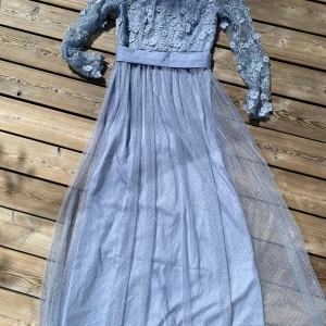 Klänning M - Blå klänning lång med tyll, broderier pärlor mm. Aldrig använd. Har dock fått några udda märken på rygg, se foto! Går säkert bort i tvätt. Ej tvättad förr. 
