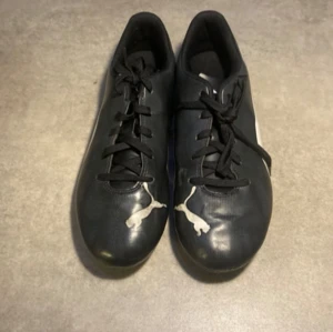 Fotbollsskor-svart - Puma fotbollsskor med vita och blåa detaljer. Skorna har lite vintage tryck så det vita ser slitet ut men den kommer så. Helt nya och oanvända dock utan prislapp 
