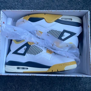 Jordan 4 Retro - Vita, gula och svarta WMNS Air Jordan 4 Retro. Gul fodring. Helt nya och oanvända inköpta 29:e juni i butik. Storleken passar inte mig, och jag får inte byta. Skorna ligger i orginalkartong. Modellen är dam, men storlekar anges för både dam och herr.