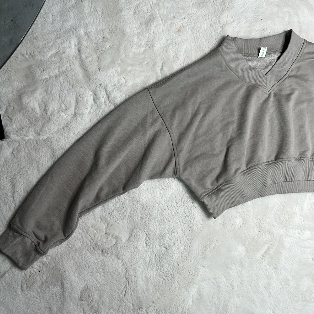 Grå croppad sweatshirt med V-ringning  Oanvänd  Saknar logga, strl: S. Tröjor & Koftor.