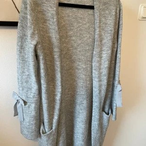 Mysig kofta  - Lång, grå kofta från Lindex med söta rosettdetaljer. Väldigt mjuk och säljer pga att den inte passar längre.  I storlek 146/152, men passar XXS/XS 🫶🏼