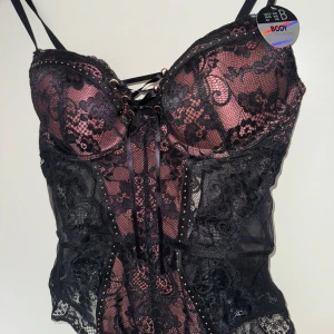 Body med spets, ny med lapp - Sexig superfin body, aldrig använd. Massa fina detaljer som snören, ringar, spets, pärlor osv, se alla bilder. Säljer pga inte min stil längre & fel storlek för mig nu. Storlek 75B. 
