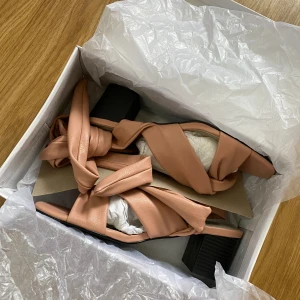 Helt nya klackskor - Helt ny klackskor från Nelly, endast testade. Säljes pga de inte kom till användning på det jag skulle på. Klackhöjd 6cm. Man knyter dem kring benen/anklarna. Djur och rökfritt hem, färgen är smutsrosa! 