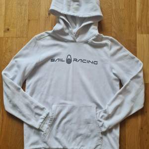 Vit hoodie från Sailracing säljes i mycket fint beg skick. Nästan aldrig använd. Hel och ren och inte tvättpåverkad. Där finns en liten fläck på underarmen men den syns inte.  (Se bild)  Rygglängd 63 Djur & rökfritt hem