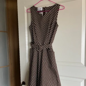 50-talsklänning i nyskick  - Jättefin 50-talsklänning i kraftig bomull med lite elastan. Längd från midjan  ca 60 cm. Brun botten med vita prickar  ( tänk Julia Roberts i Pretty Woman).  Använd vid ett tillfälle. 