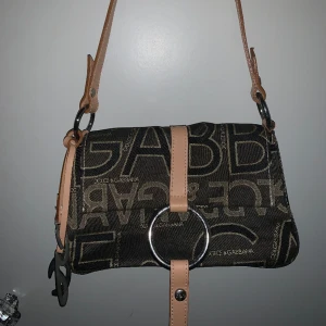 Dolce & Gabbana handväska - Denna handväskan från Dolce & Gabbana är en liten men rymmlig handväska. Detta är en äldre model, oklart vilket år den kom ut. Vintage märkes väska i mycket bra skick. Inga skador, fläckar eller liknande på ytan eller inne i. För mer info - kontakta!