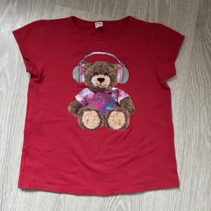 Röd babytee nallebjörn - Söt babytee med en nallebjörn på🥰 I fint skick. Skriv privat om ni har frågor 💕Den är i barnstorlek men passar mig som en babytee som brukar ha M
