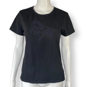 Svart Tee - I fint skick, storlek M. Snyggt hästmotiv, som glittrar i solen och är mer diskret i mörkret! MÅTT: Axel till axel 40cm, ärmlängd 16cm, armhåla till armhåla 45cm & längd 57cm 