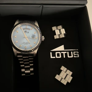 Lotus klocka - En fin Day-date klocka från märket Lotus. Den har några få skrapsår vilket gör att priset minskas en del. Det går att fixa genom polering. Funkar perfekt.