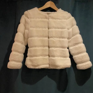 Super söt fluff jacka - Jätte söt fluffjacka med pärlor, använd ett fåtal gånger och säljer nu då den är för liten. Obs färgen på bilden är lite missvisande då den är vitare i verkligeheten!