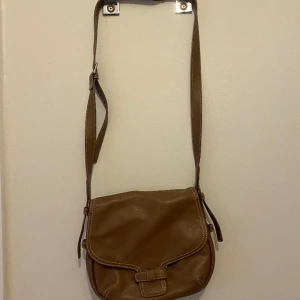 Axelväska  - Fin axelväska med retro känsla. Använd ett fåtal gånger. Längden är justerbar. Det finns två små fack inne i väskan och ett på baksidan med. Osäker på om det är äkta eller fejk läder (troligen faux)