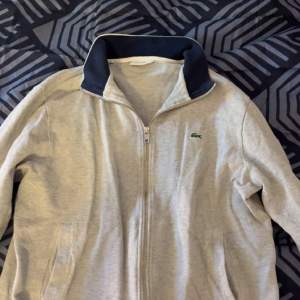 Lacoste full zip - Storlek small - skick: 8/10, använd lite i sommras. färg: grå/blå - inget följer med - tveka inte på att skriva ifall ni har några frågor eller funderingar. Nypris 1299.