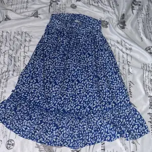 En blå kjol med blommigt mönster som går ner lite under knäna. Använd ett fåtal gånger, skriv vid frågor.