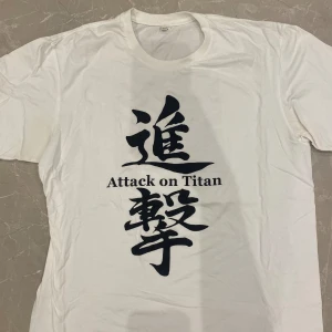 Attack on titan -  En vit t-shirt och med den animerade ”Attack on titan”  loggan på fram och baksidan 