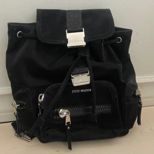 Steve Madden ryggsäck  - Svart bwilder ryggsäck från märket Steve Madden , inte använd , passar att ha skoldator i eller använda som resväska. Tre ytterfickor (två på sidorna) och två fickor inuti. 