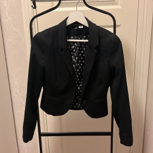 Kort kavaj  - Svart kort kavaj med en knapp. Katt finns i hemmet.