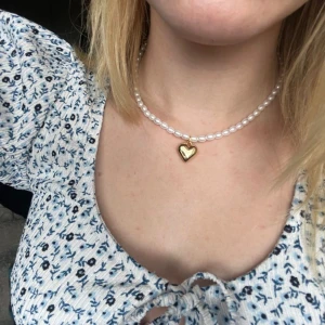 Egengjort pärlhalsband - Egengjort pärlhalsband med vita pärlor. Halsbandet har en guldig berlock som avbildar ett hjärta. 