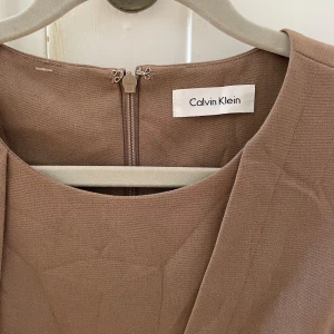 Beige klänning från Calvin Klein - En elegant beige klänning från Calvin Klein. Den har typ en båtringning? och en dragkedja på baksidan. Slutar strax ovanför knäna på mig som är 1,63! finns ingen storlek på den då jag köpt den second hand men passar mig med S/M. 
