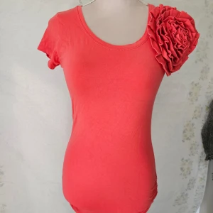 Röd topp från Awsarre - En korall vardags klänning från Awsarre med en stor volangdetalj på vänster axel. Klänningen har korta ärmar och en rund halsringning.