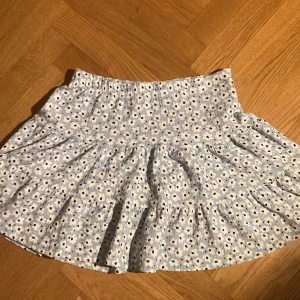 Blommig kjol från lager 157 - Säljer en ljusblå blommig kjol från lager 157, är i bra skick, enda märkvärdiga är att lappen är nära att ramla av (se bilder på lappen). I storlek 160 på avdelning barn, säljer pga oanvänd sen ca vår 2023. Köpare står för frakt.